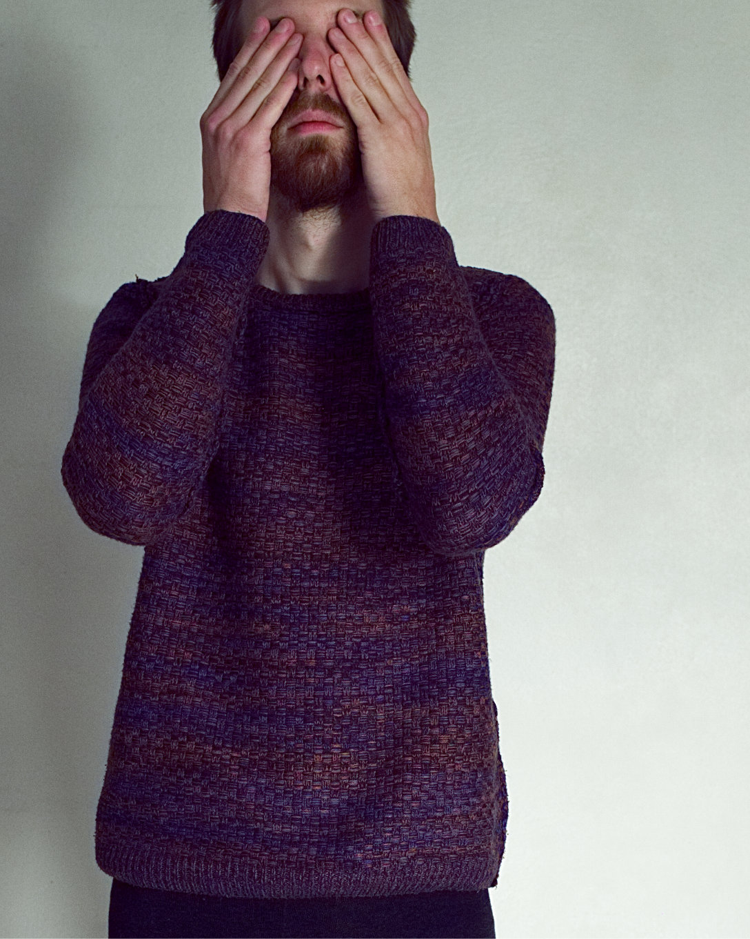 Male model wearing a dark sweater covers his eyes with his hands