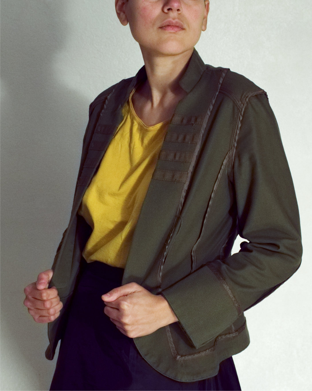 Model wears a olive green jacket and a yellow shirt, their eyes are outside the frame hidden