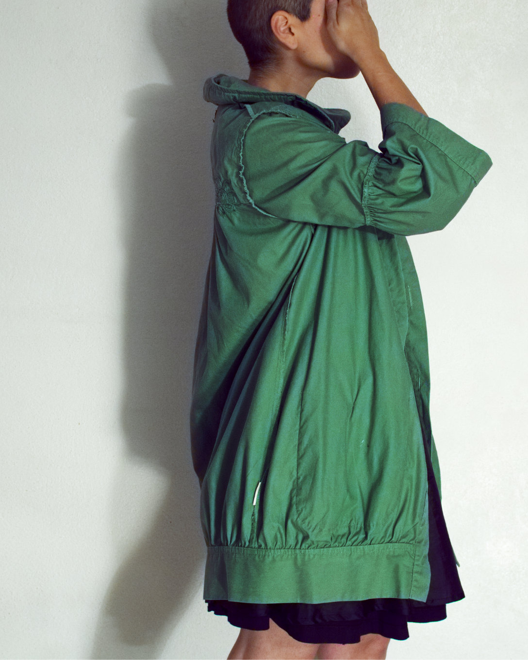 Model wears a green light coat, side view, coving their eyes