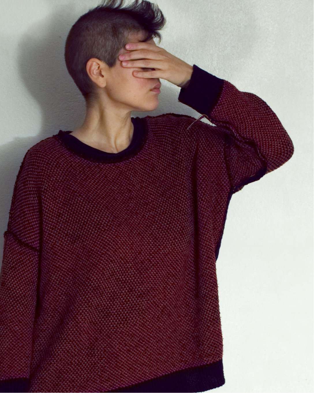 Model wears a red and black sweater, coring their eyes