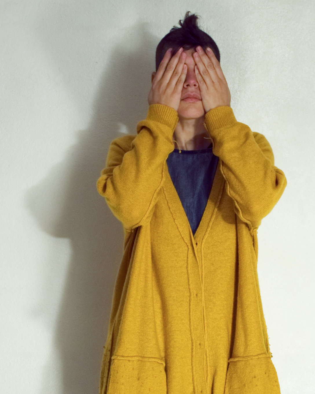 Model wear a yellow long cardigan while covering their eyes